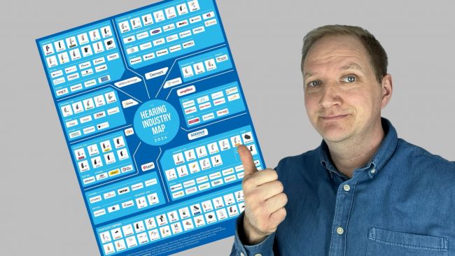 Maximilian Bauer mit einer Map aller Hörgeräte Hersteller weltweit im Hintergrund